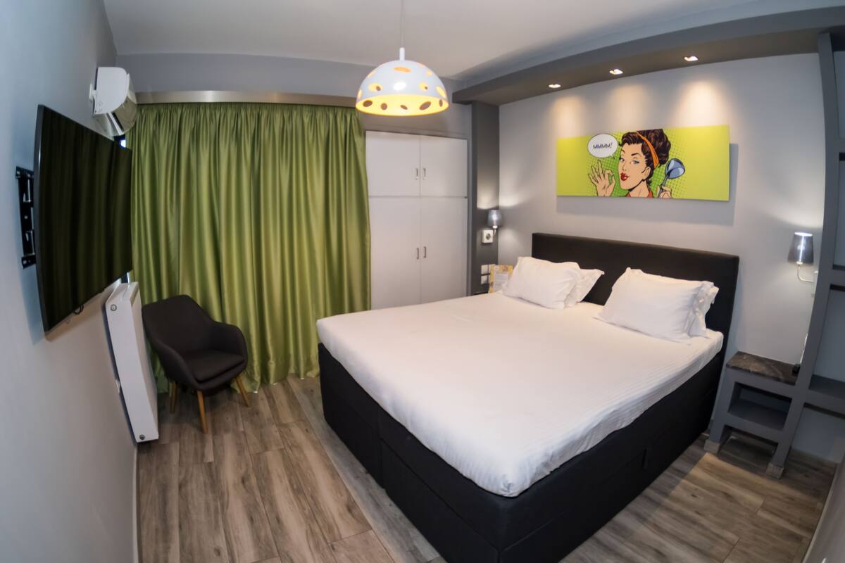 Una habitación de hotel moderna con una cama grande, un escritorio, una silla, un armario y un cuadro en la pared.