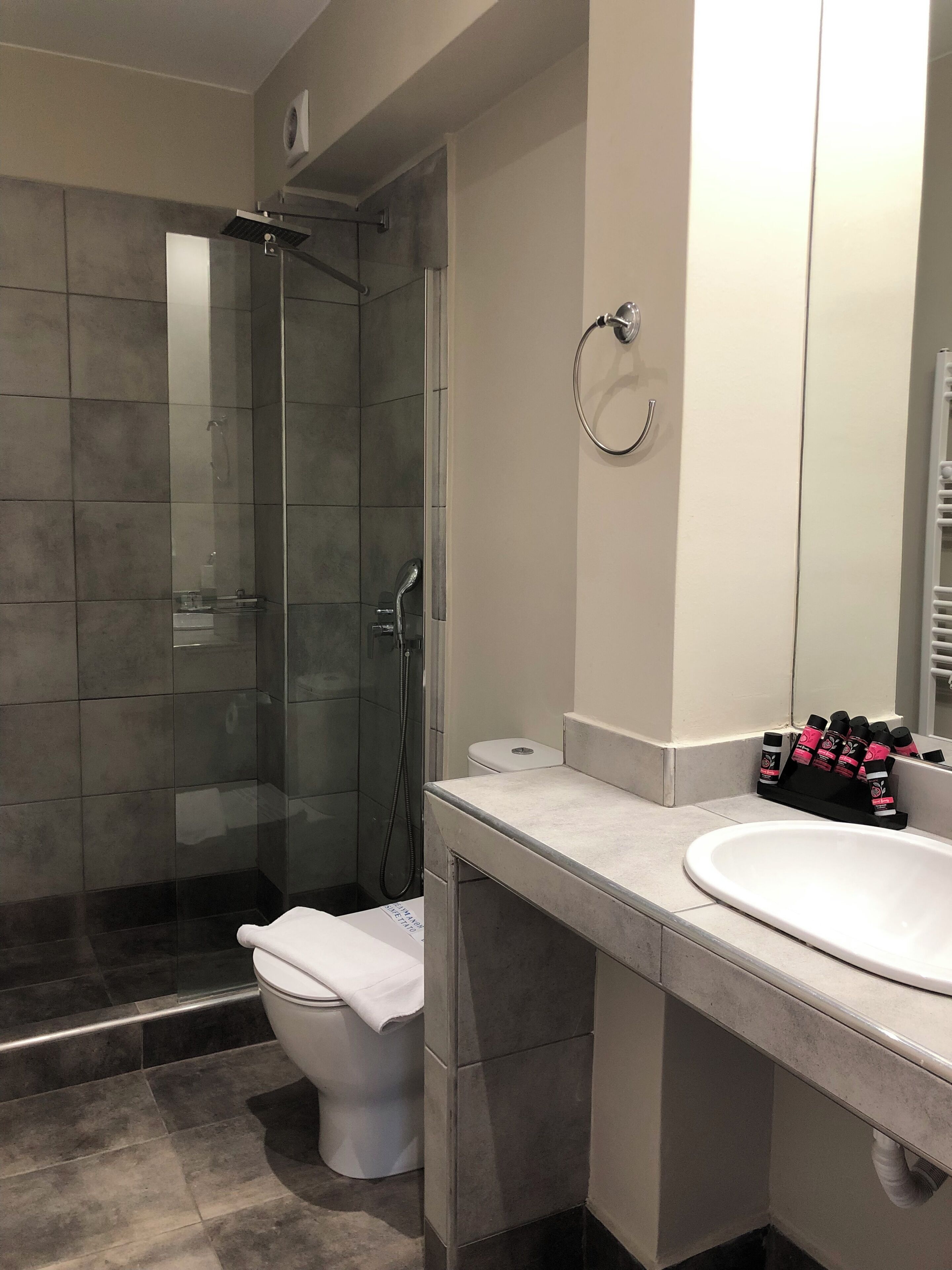 Un baño moderno con ducha de vidrio, inodoro blanco y tocador con lavamanos y espejo.