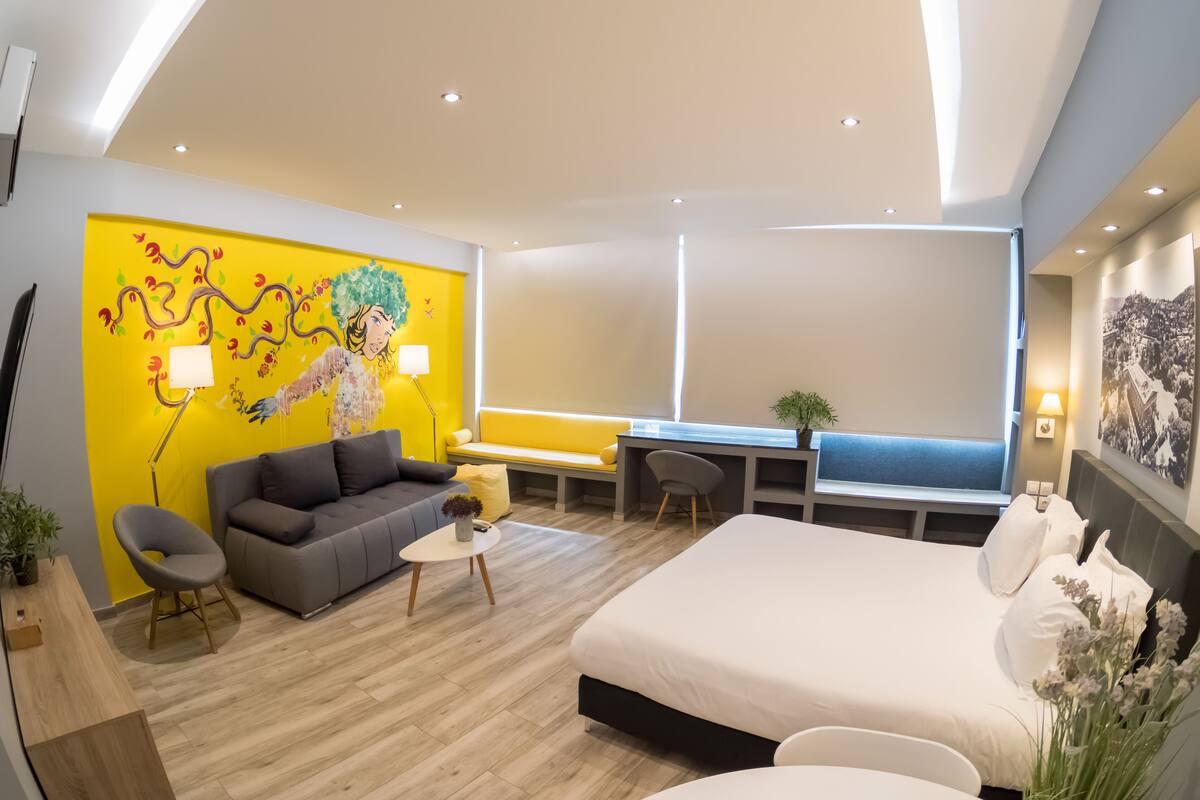Habitación de hotel moderna con una cama grande, un sofá, un escritorio y una pared amarillo brillante con un mural.