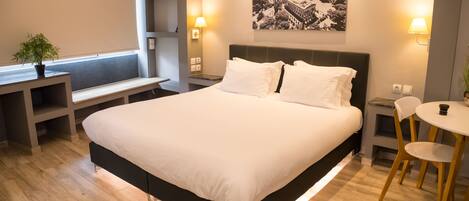 Una habitación de hotel moderna con una cama grande, mesitas de noche, un escritorio pequeño y una silla.