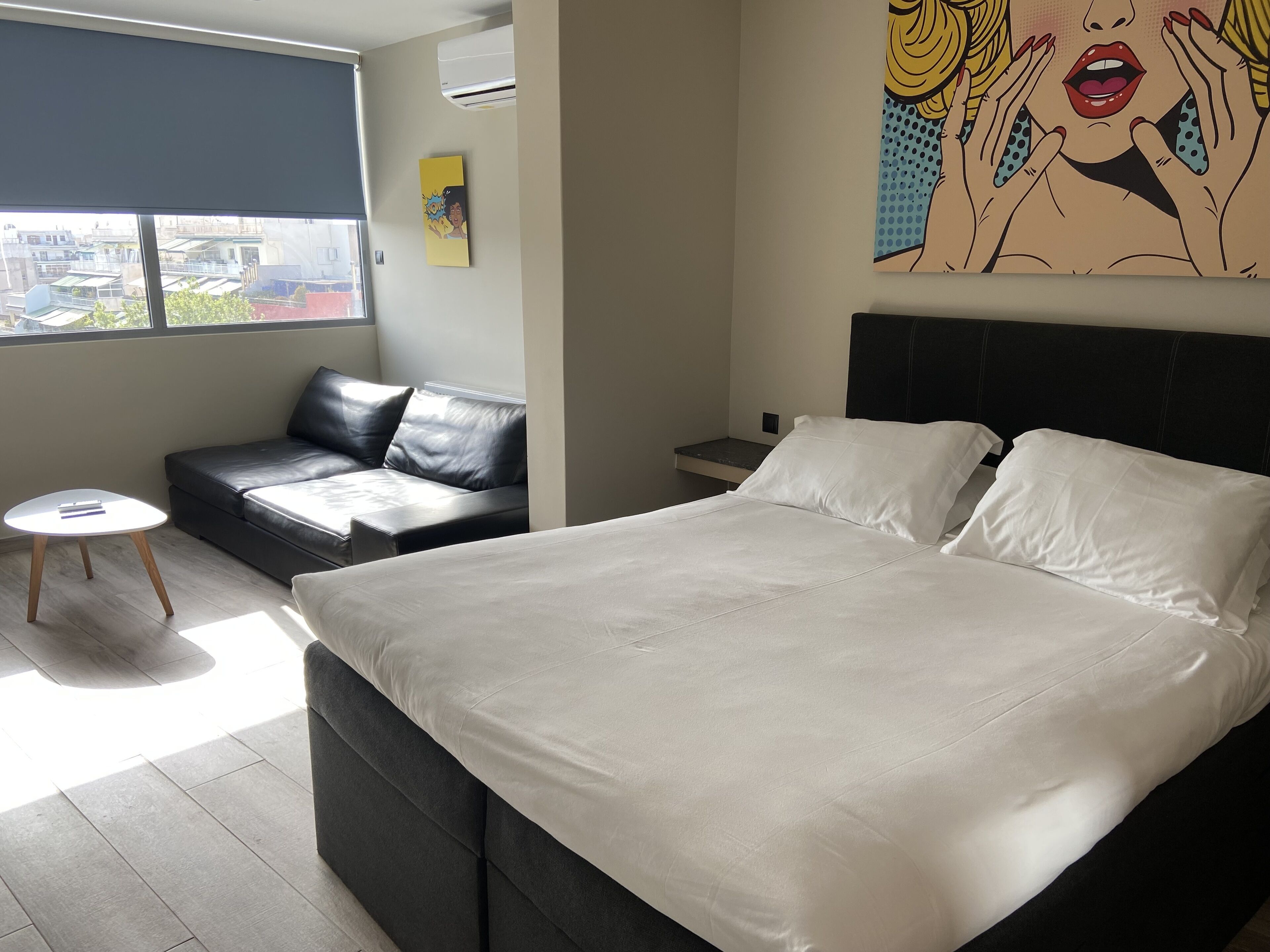 A modern hotel room with a large bed, a sofa, a small table, and a city view.