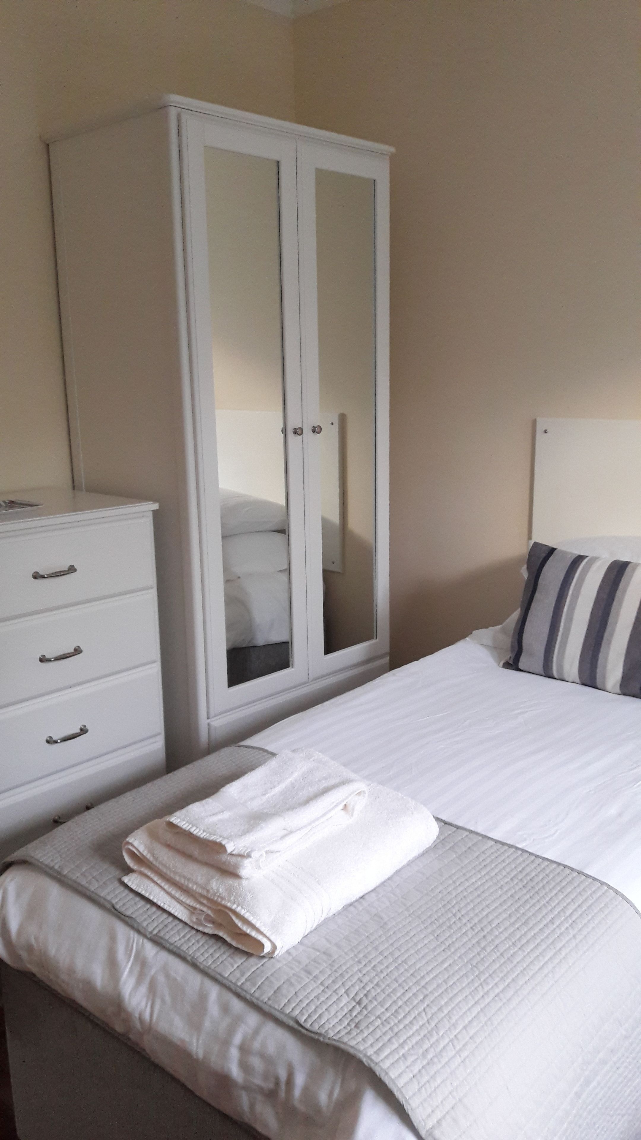 Une chambre à coucher avec un lit, une armoire blanche, une table de chevet et un coussin à rayures.