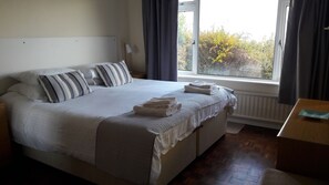 Una cama bien hecha con almohadas, una ventana con cortinas y una mesita de noche de madera con una lámpara.