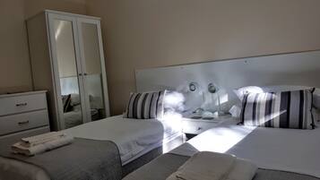 A hotel room with two beds, a wardrobe, a bedside table with lamps, and a mirror.