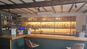A bar area with a wooden counter, two bar stools, and a variety of bottles and glasses on shelves. - The North Hill Hotel, Colchester (Colchester)