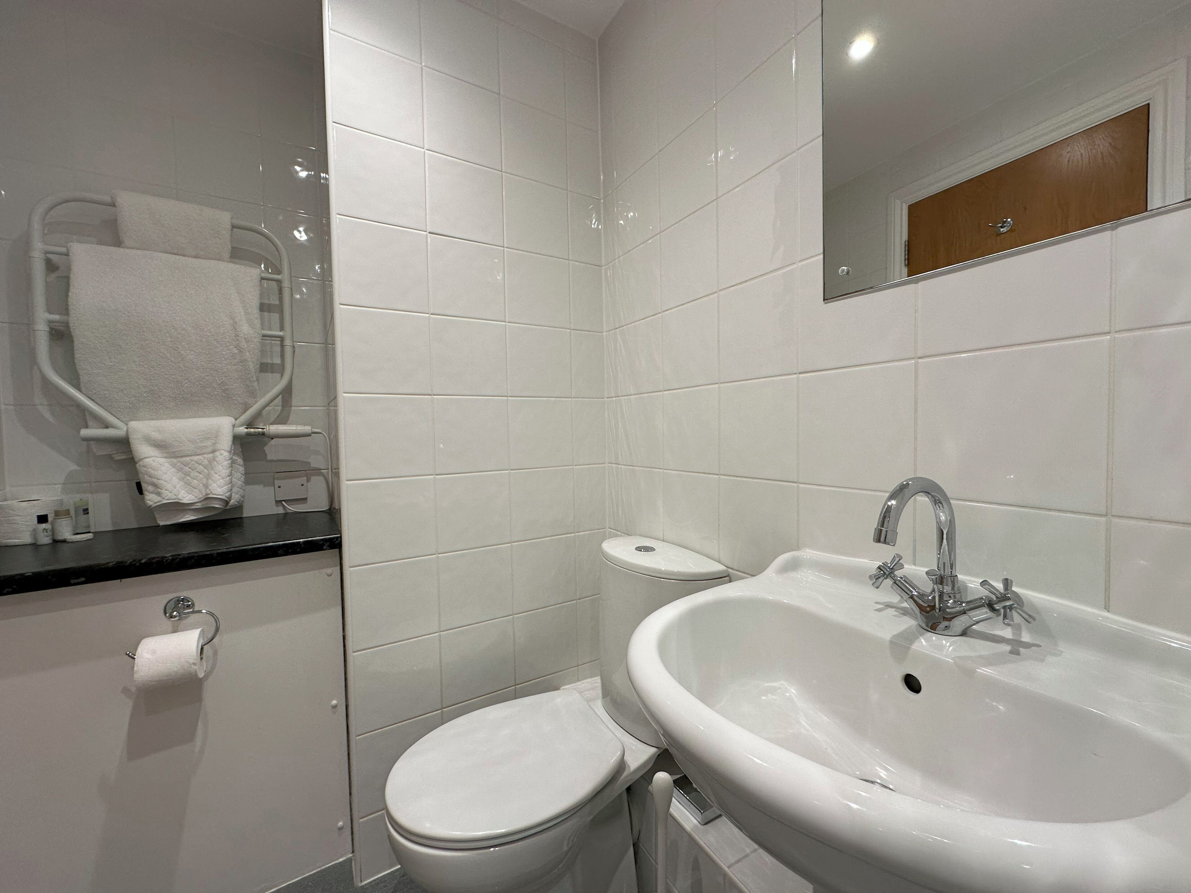 Un baño moderno con lavamanos, inodoro y zona de ducha blancos.
