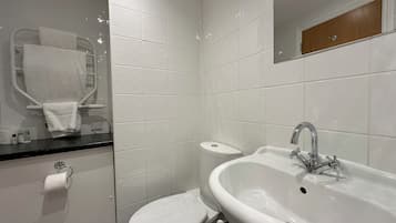 Un baño moderno con lavamanos, inodoro y zona de ducha blancos.