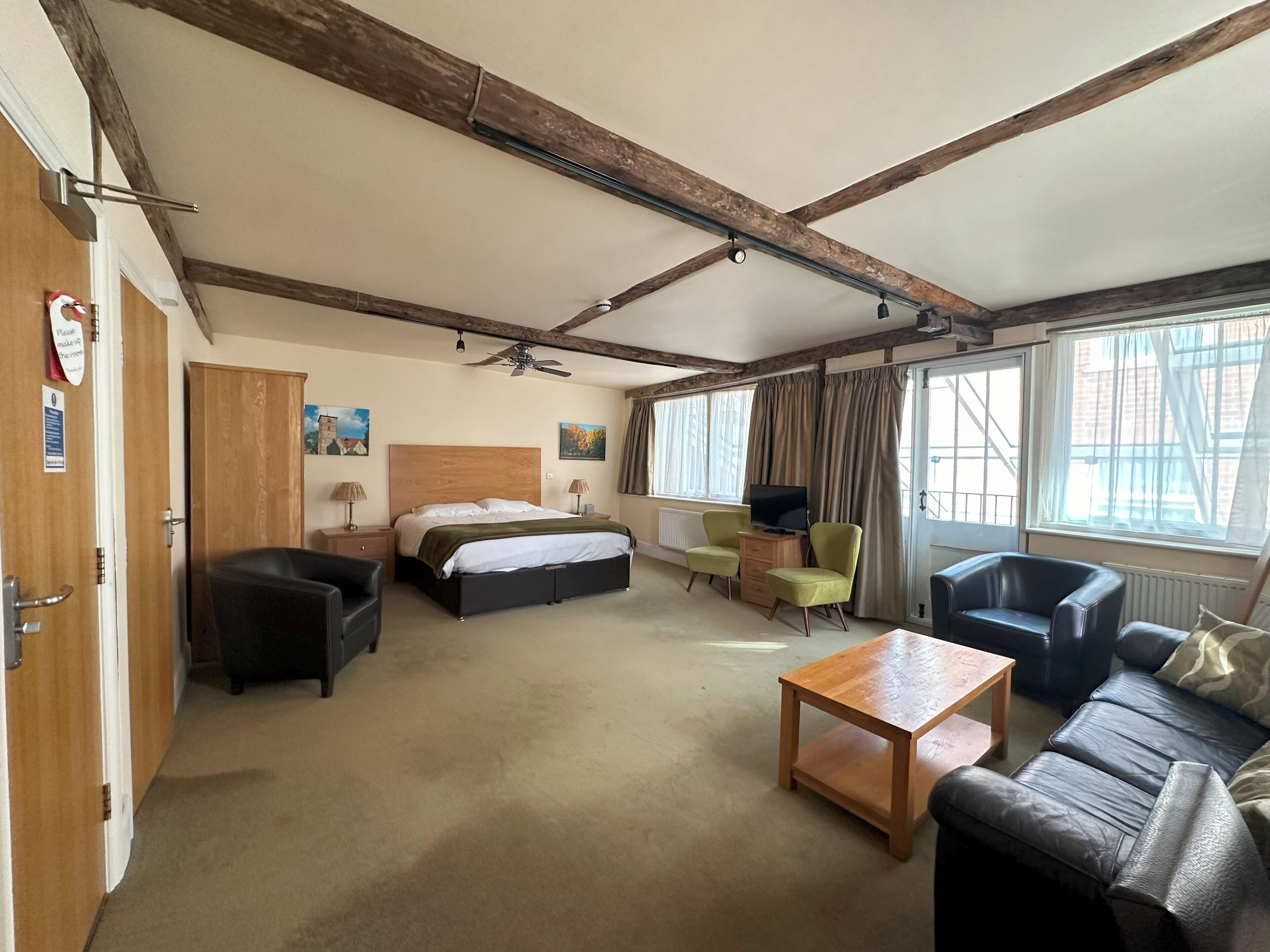 A hotel room with a bed, two armchairs, a sofa, a wooden coffee table, a TV, and a ceiling fan.