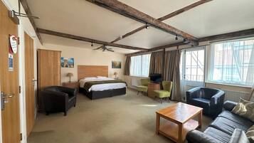 A hotel room with a bed, two armchairs, a sofa, a wooden coffee table, a TV, and a ceiling fan.