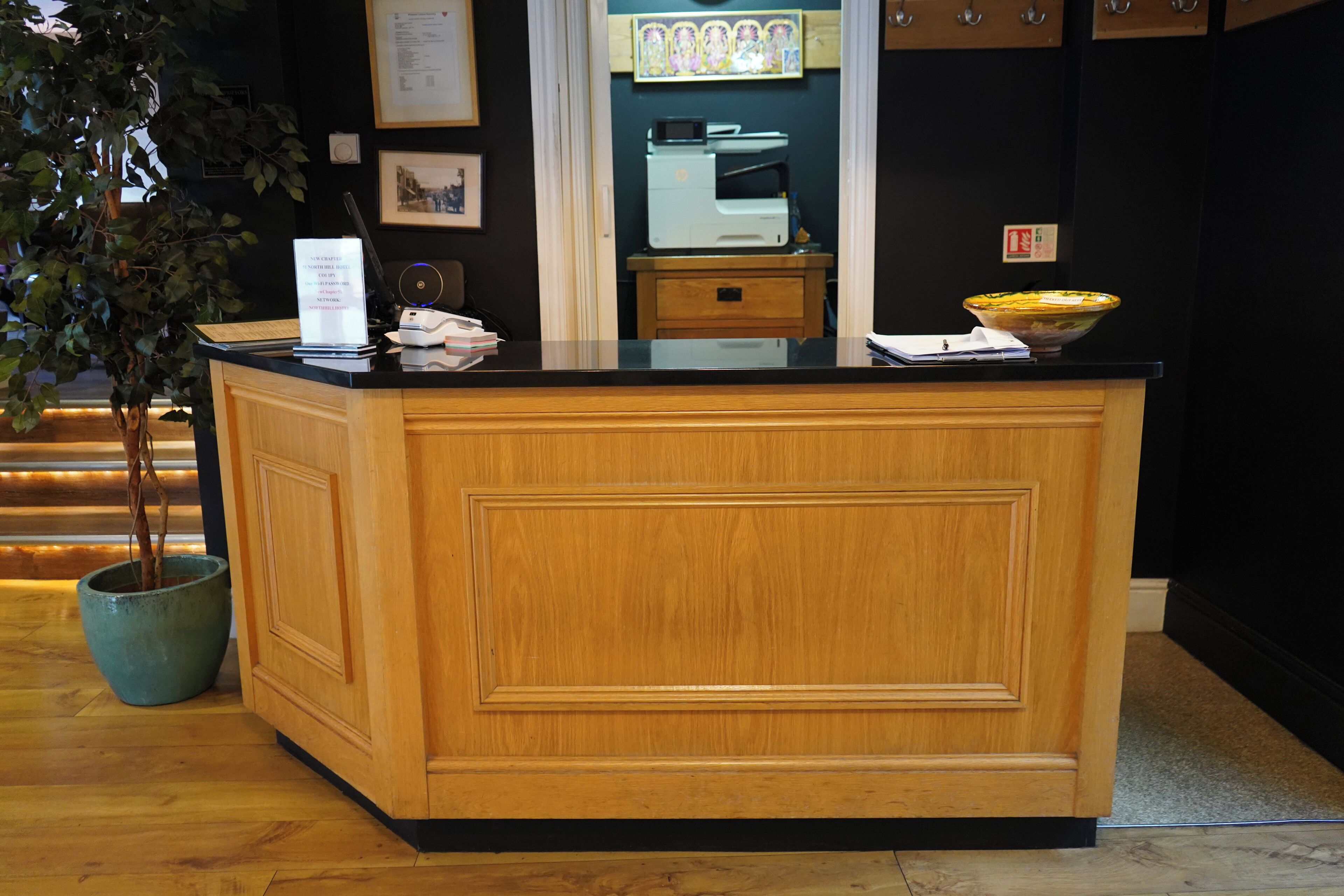 A reception desk with a wooden finish, a potted plant, a printer, and a bowl on the counter.