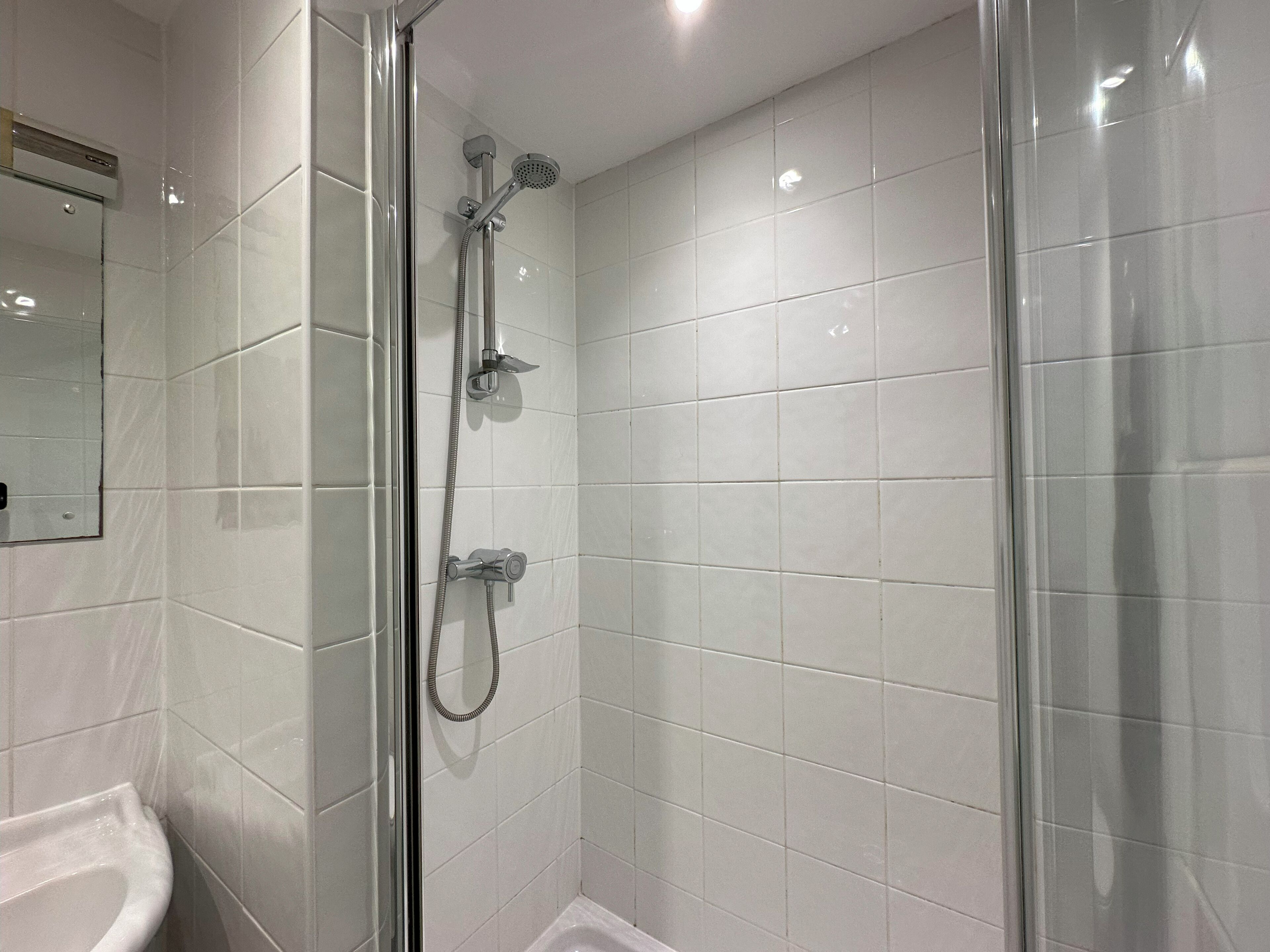 A modern bathroom with white tiles, a glass shower enclosure, and a white sink.