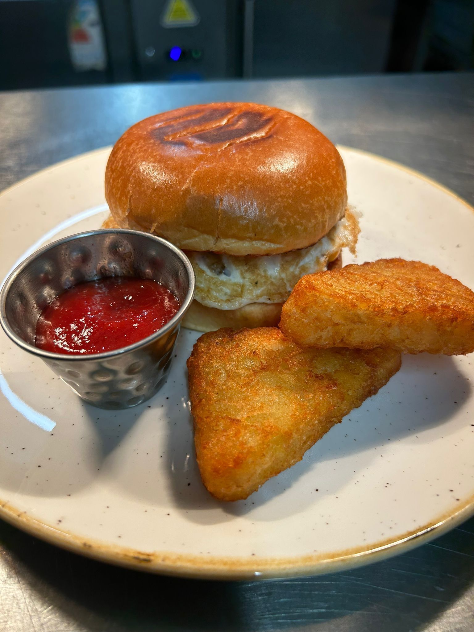 Een bord met een sandwich, een klein metalen bekertje ketchup, en twee gebakken snacks.