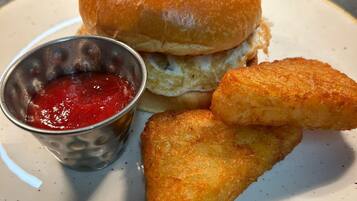 Een bord met een sandwich, een klein metalen bekertje ketchup, en twee gebakken snacks.