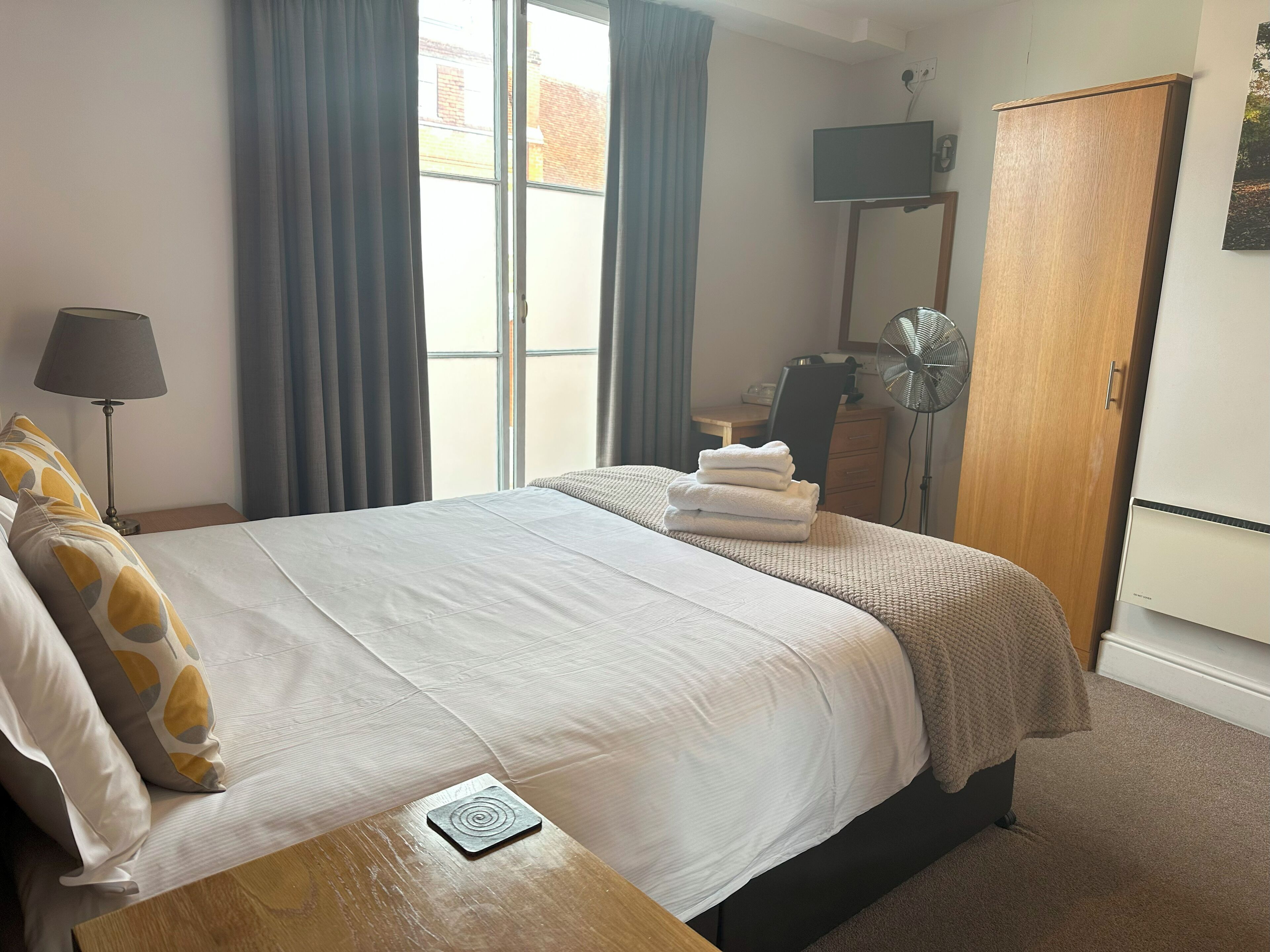 Une chambre d’hôtel équipée d’un lit, d’un bureau, d’une chaise, d’une télévision, d’une armoire et d’une fenêtre avec des rideaux.