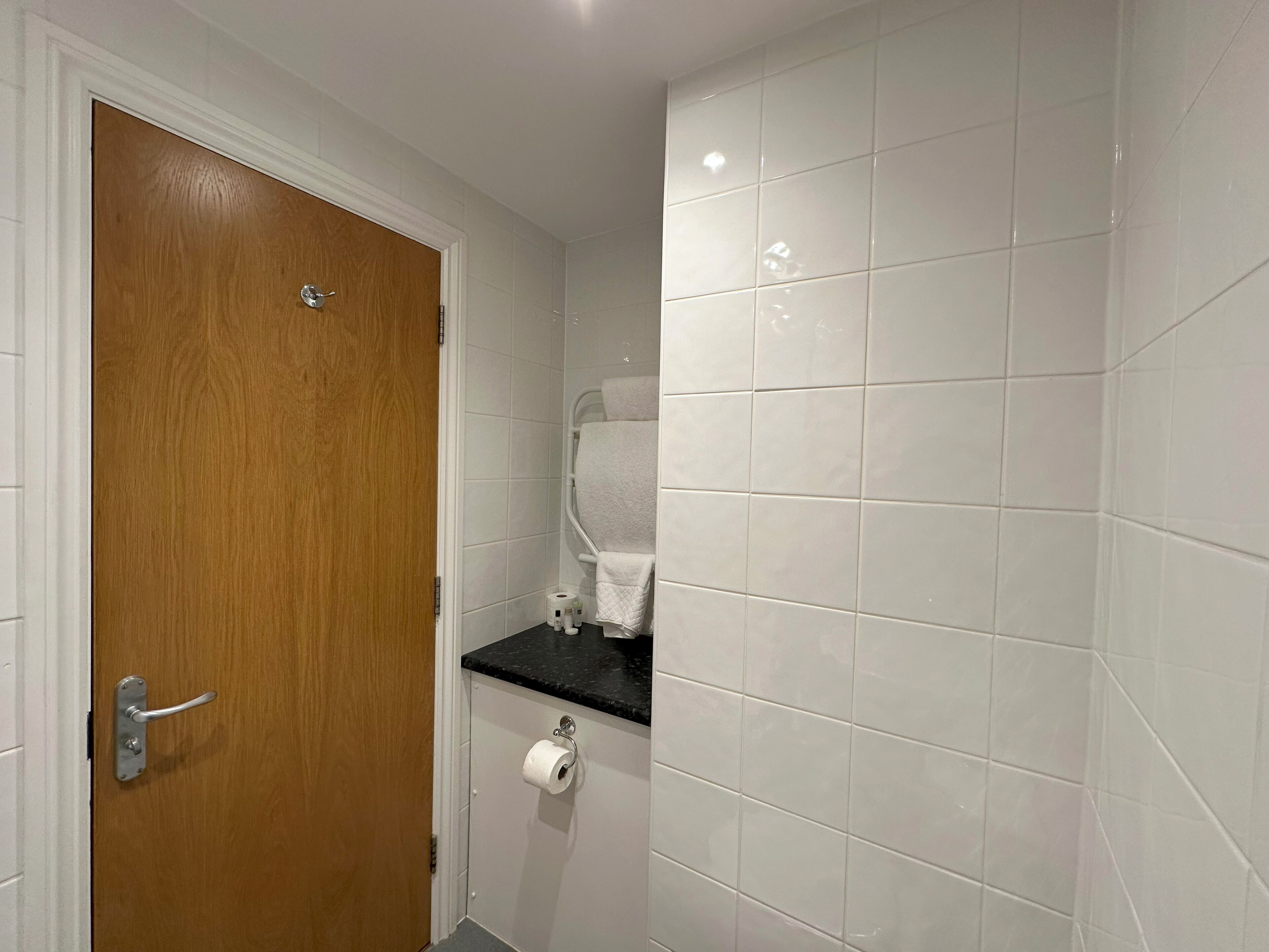 A bathroom with white tiles, a wooden door, a black countertop, and a towel rack.