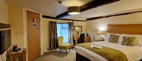 A hotel room with a large bed, a desk, a chair, a TV, and a window with curtains.