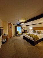Habitación de hotel con una cama grande, un escritorio, una silla, un televisor y una ventana con cortinas.