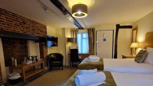 A hotel room with a brick fireplace, two beds, a desk with a chair, and a television mounted on the wall. - The North Hill Hotel, Colchester (Colchester)