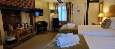 A hotel room with a brick fireplace, two beds, a desk with a chair, and a television mounted on the wall.