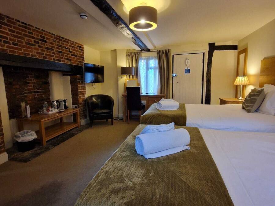A hotel room with a brick fireplace, two beds, a desk with a chair, and a television mounted on the wall.