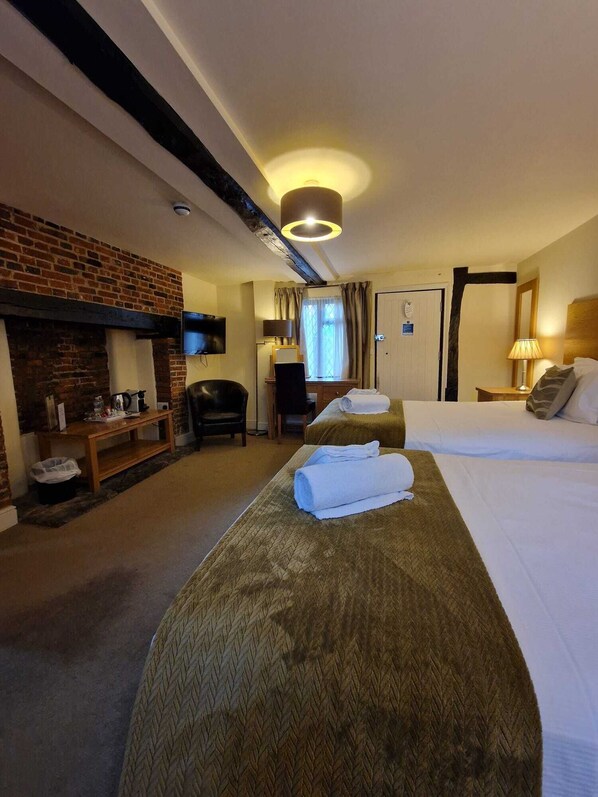 Habitación de hotel con chimenea de ladrillo, dos camas, un escritorio con una silla y un televisor montado en la pared.