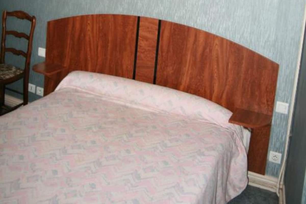 Ein Schlafzimmer mit einem hölzernen Kopfteil, einem Bett mit gemustertem Überwurf, zwei Wandleuchten und einem Holzstuhl.