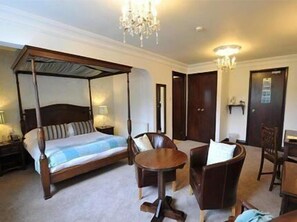 A four-poster bed with a canopy, a round wooden table, and two armchairs in a hotel room.