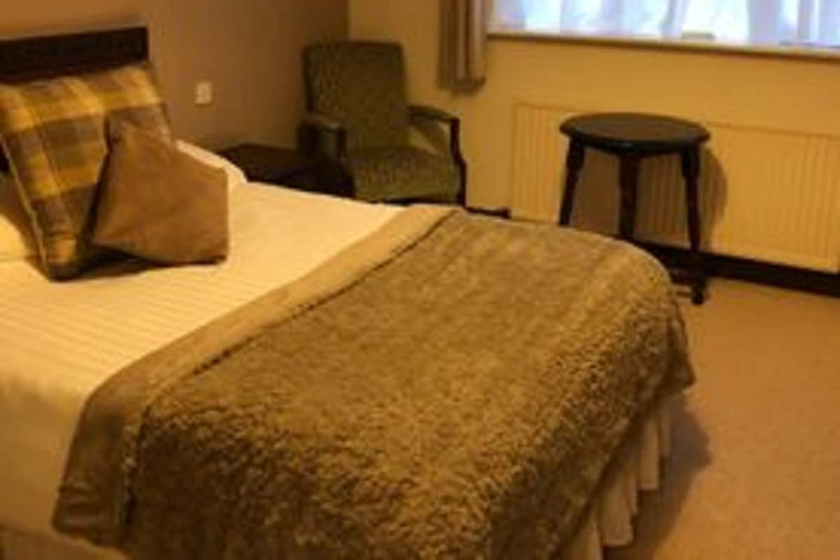 A hotel room with a bed, a chair, a small table, and a window with curtains.