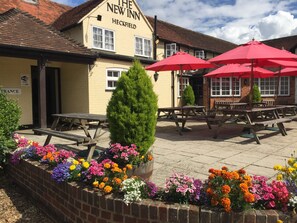A traditional pub named 'The New Inn' with outdoor seating and a variety of colorful flowers in the foreground.