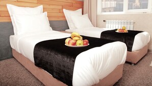 A hotel room with two beds, a wooden headboard, a city view, and a fruit plate on the beds. - Small Hotel Bishkek (Bishkek)