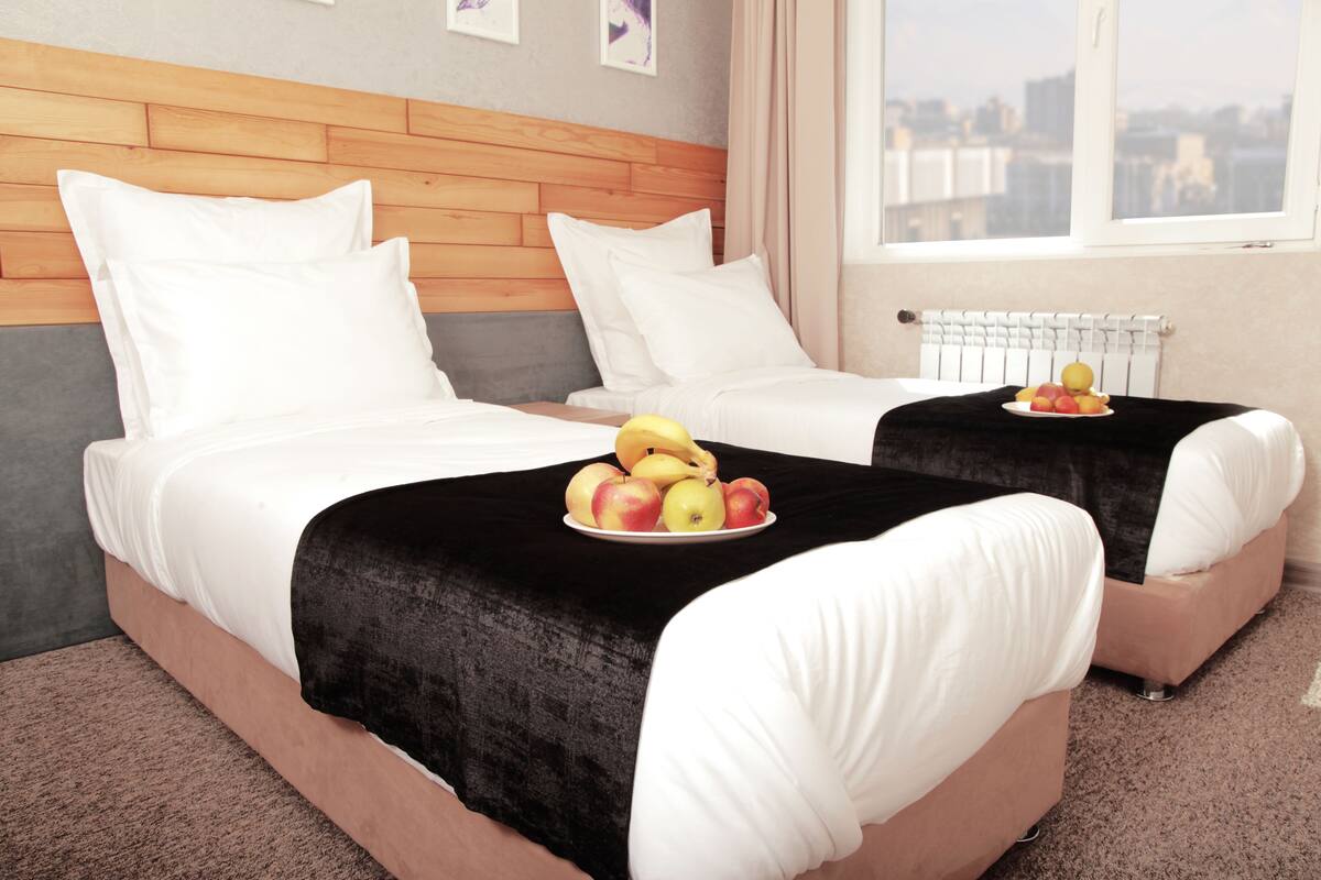 A hotel room with two beds, a wooden headboard, a city view, and a fruit plate on the beds.