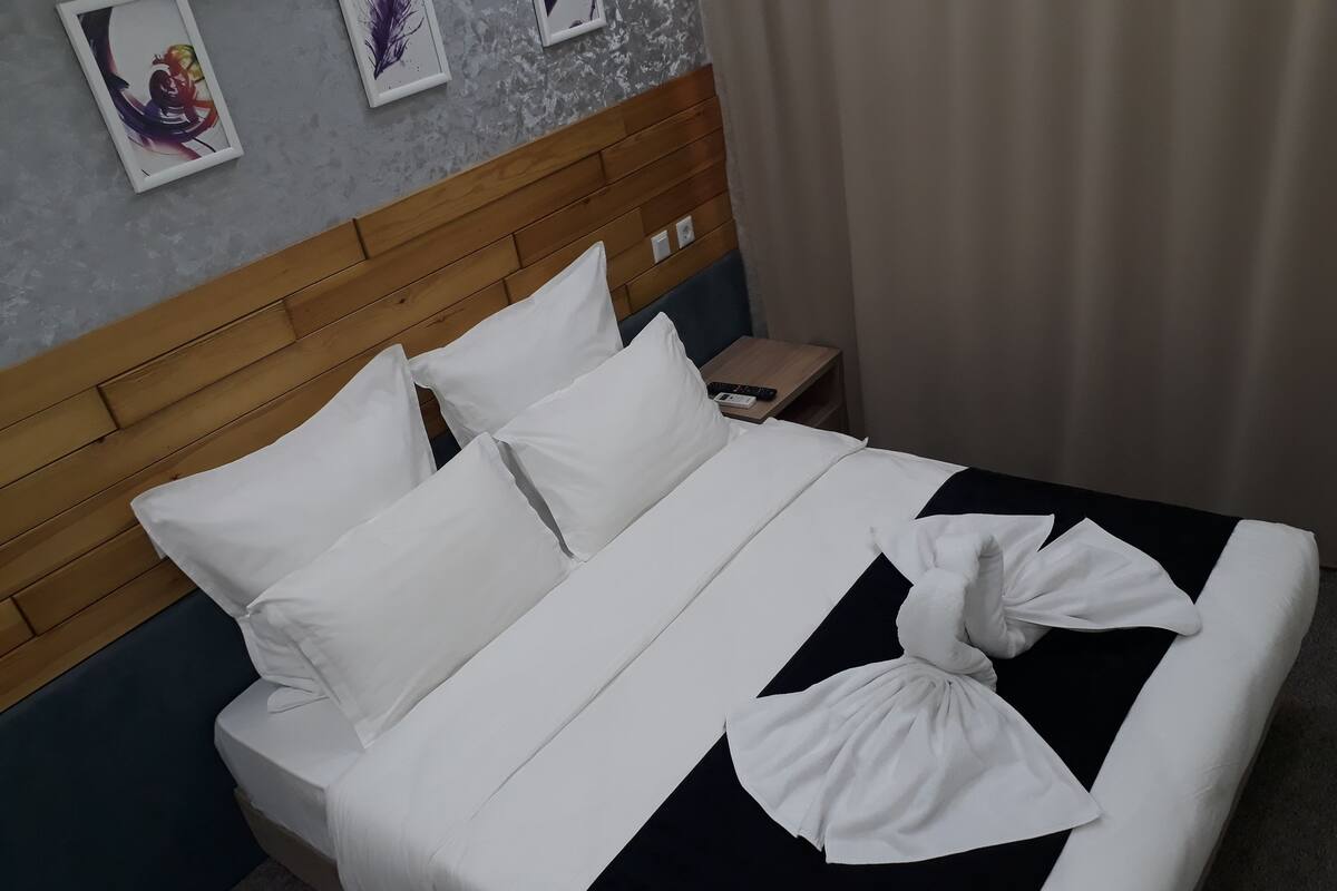 A neatly made bed with white and black bedding, a wooden headboard, and a remote control on a bedside table.