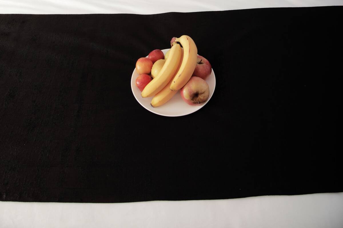 A neatly made bed with white linens and a black bedspread, a plate of fruit on the bed, and a modern headboard with wall-mounted lights.