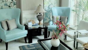 A modern living room with two light blue armchairs, a white armchair, a black coffee table, and a decorative vase. - Hotel Palm Greens (New Delhi)