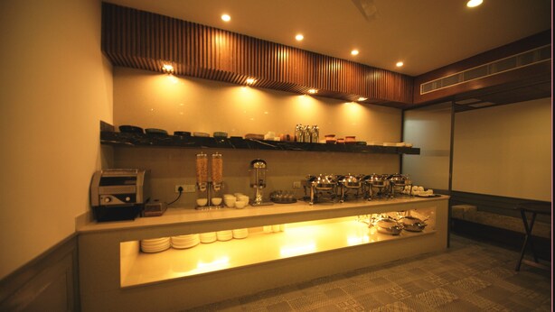 A buffet setup with various dishes and utensils on shelves, a coffee machine, and a cash register. - Hotel Palm Greens (New Delhi)
