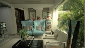 A modern living room with a blue sofa, white armchairs, a coffee table, and a large vase. - Hotel Palm Greens (New Delhi)