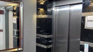 A modern elevator with a metallic finish, flanked by black marble walls with white veining. - Hotel Palm Greens (New Delhi)