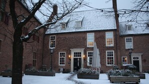 A brick building with a snow-covered courtyard, a central entrance, and a bench.