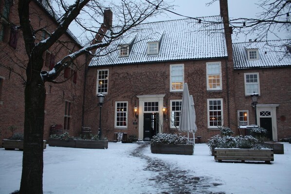 Un edificio de ladrillo con un patio cubierto de nieve, una entrada central y un banco.