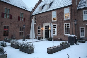 A snow-covered courtyard with brick buildings, outdoor seating, and planters. - De Hemel Hotel Suites Nijmegen (Nijmegen)