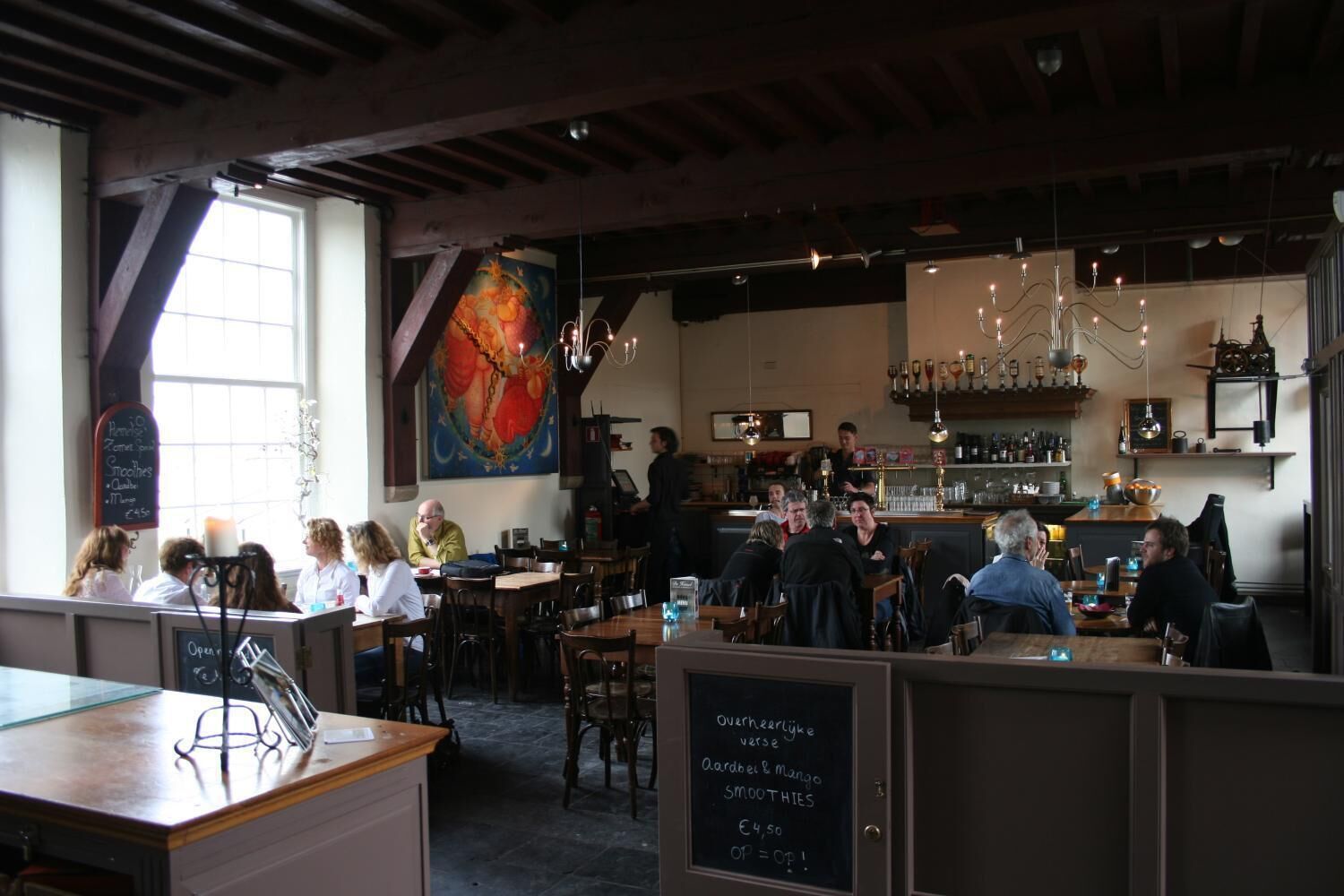 Een restaurant met houten balken, een bar en gasten die aan tafels zitten.