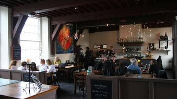 Een restaurant met houten balken, een bar en gasten die aan tafels zitten.