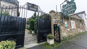 L’entrée d’un hôtel, avec un portail en fer forgé, un mur en pierre et une enseigne indiquant le nom de l’hôtel et les services proposés.