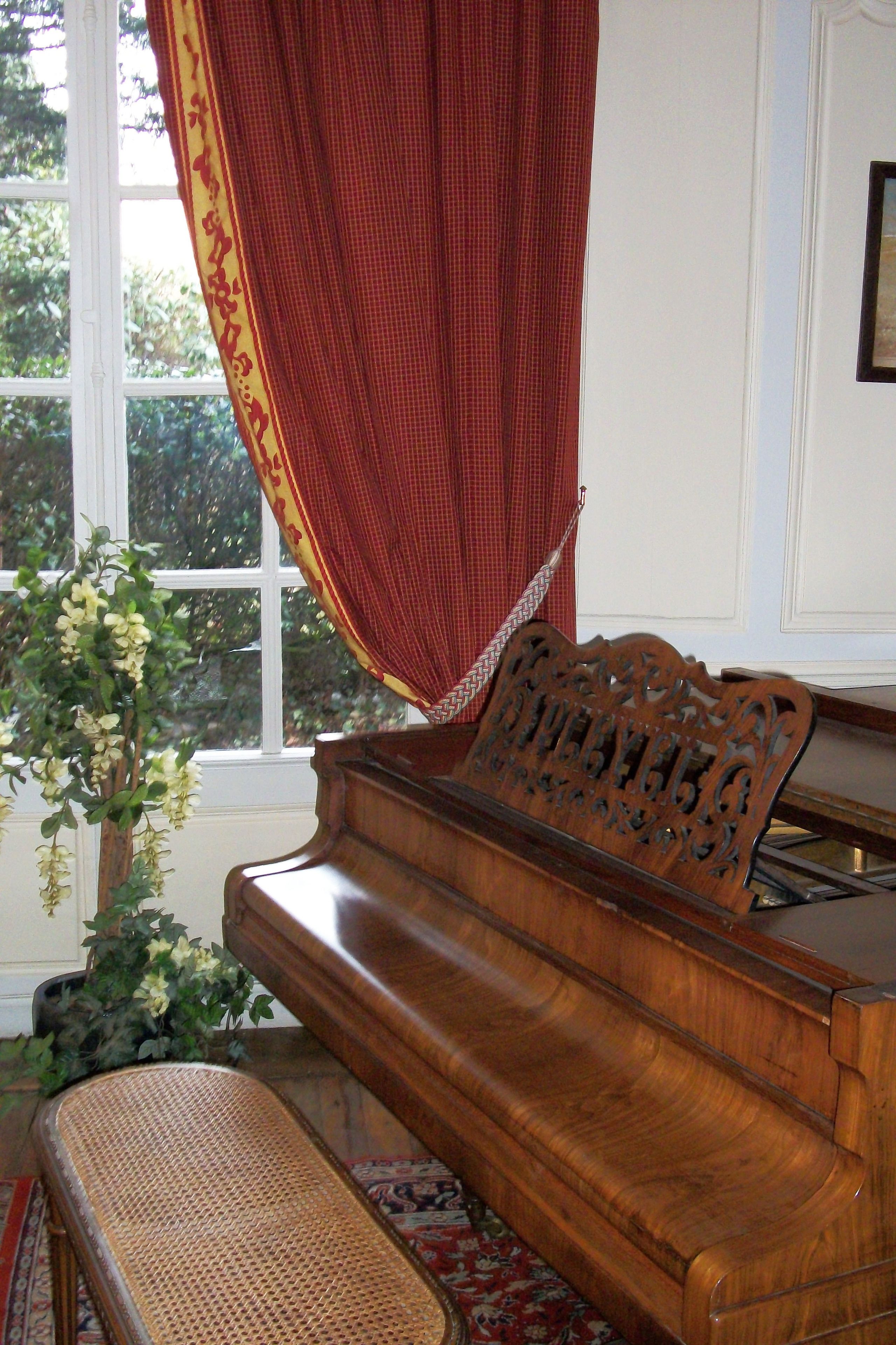Un piano de cola imponente con un banco, ubicado cerca de una ventana con cortina roja.