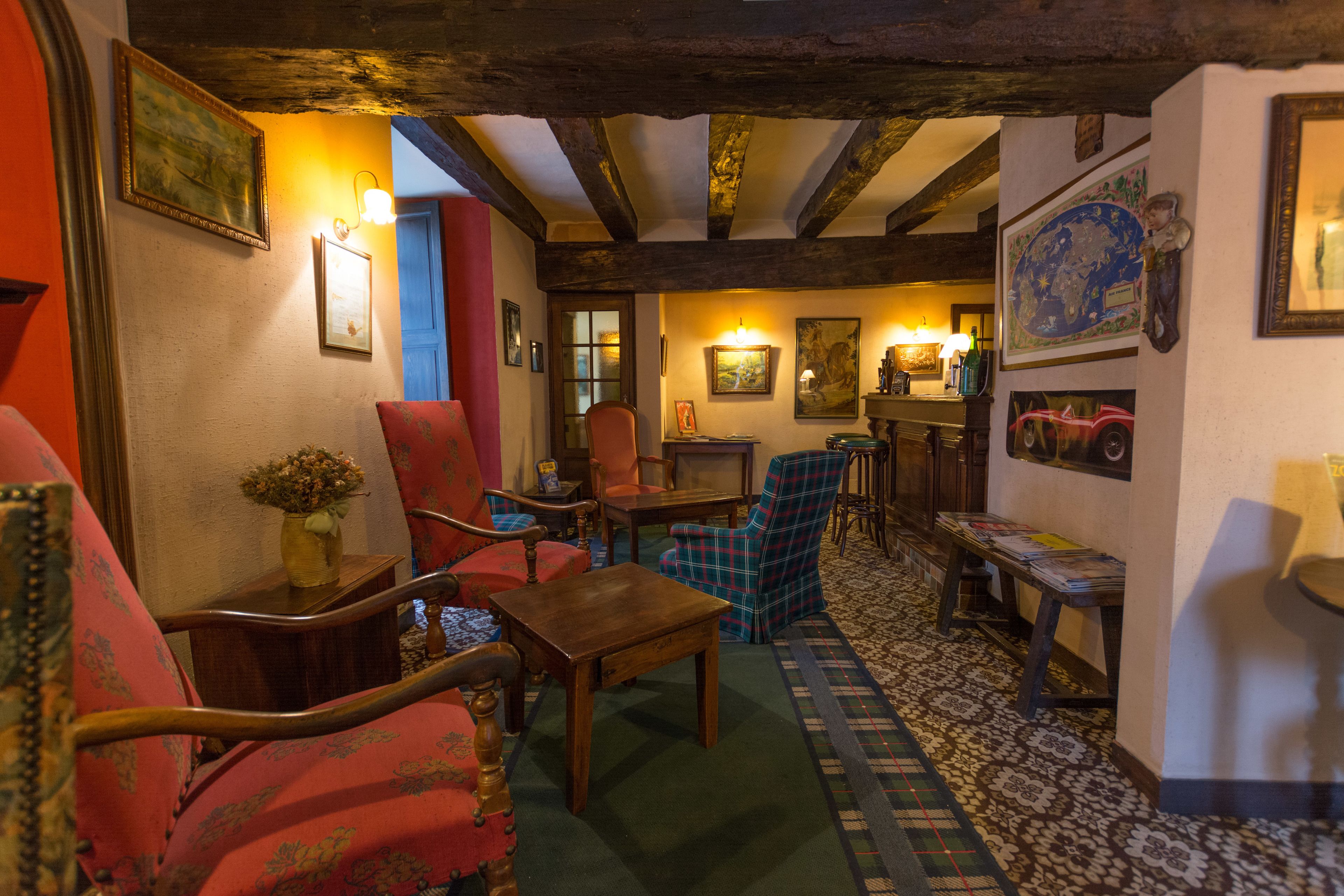 A cozy room with wooden beams, a patterned carpet, and a mix of seating including a red armchair, a plaid armchair, and a wooden table.