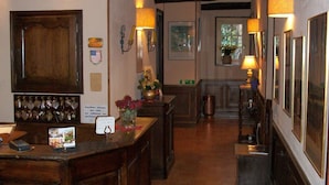 Un hall d’auberge traditionnel avec des poutres en bois, un comptoir d’accueil, un tapis et des tableaux encadrés aux murs.