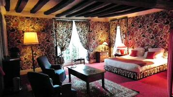 A bedroom with a bed, two chairs, a table, and a lamp.