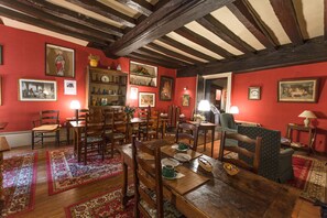 A dining area with wooden furniture, a red wall, and various framed pictures. - Relais Cicéro (La Flèche)