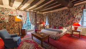 Une chambre à coucher avec un lit, une chaise, une table et une fenêtre avec des rideaux.