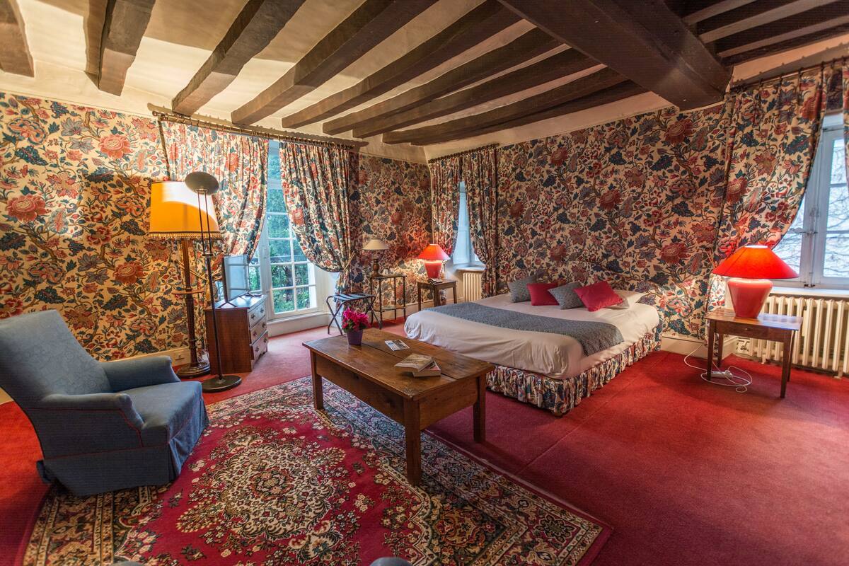 A bedroom with a bed, a chair, a table, and a window with curtains.